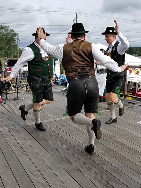 Schuhplattler dancers in lederhosen and green vests dancing on the stage